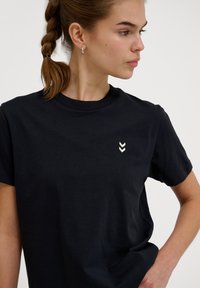 Sort bomulds T-shirt med rund hals, korte ærmer og et lille broderet chevron-design i hvidt på venstre brystområde.