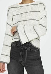 Biały sweter z dzianiny z szarymi, poziomymi paskami, szerokimi rękawami i dekoltem typu łódka. W zestawie z ciemnoszarymi, wysokim stanem jeansami.