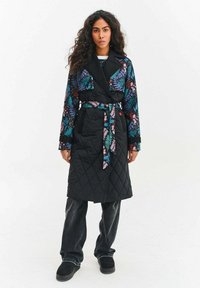 Čierny prešívaný trenčkot s kvetinovým vzorom na rukávoch a golieri, s ladiacim opaskom, dvoma gombíkmi a bočnými vreckami.