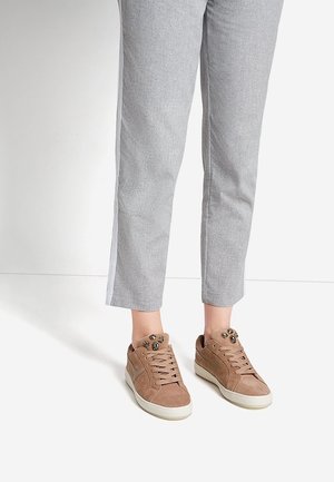 Bruine suede sneakers met tan veters en decoratieve studs op de tong, gecombineerd met lichtgrijze enkelbroek met een zijstreep.