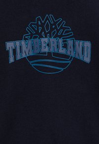 Sudadera azul marino que presenta un gran logo azul de Timberland y un gráfico de árbol estilizado, impreso en un tejido suave con una textura lisa.