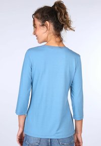 Hellblaues Langarmhemd mit rundem Halsausschnitt und dreiviertellangen Ärmeln, das ein schlichtes Design mit strukturiertem Stich um den Hals hat.