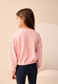 Felpa rosa con motivo a fiocco, collo rotondo ed elastico in vita. Abbinata a leggings blu navy a coste, vista da dietro.