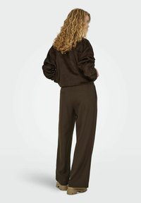 Brūna zamša jaka ar platiem piedurknēm, kopā ar tumši brūnām, augsta vidukļa taisnām biksēm. Biezas bēša platformas kurpes.