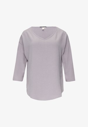 Blouse longue à manches longues de couleur violet clair avec décolleté en V et tissu texturé à l'avant, étiquetée taille petit, présentée sur fond blanc.