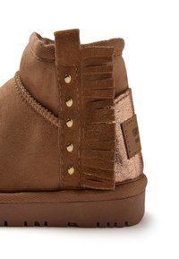 Botín de ante marrón con un acento metálico cobre texturizado, franjas decorativas y detalles de tachuelas doradas en el lateral. Suela de goma con agarre.