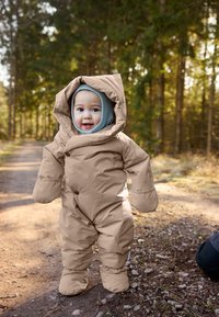 Hnedý nadýchaný snowsuit s veľkou kapucňou, nadrozmernými rukavicami a modrou základnou vrstvou s kapucňou. Umiestnený na lesnej ceste s jemným slnečným svetlom prenikajúcim cez stromy.