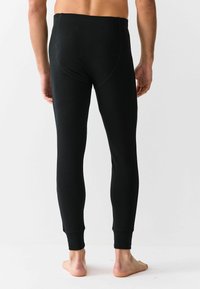 Leggings termici neri con una texture a coste, design aderente e polsini alla caviglia, mostrati di spalle su una modella scalza.