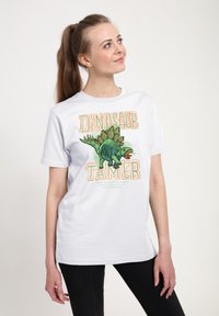 Hvid bomulds t-shirt med et grafisk motiv af en dinosaur og teksten "Dinosaur Tamer" i orange og grøn. Korte ærmer, afslappet pasform.