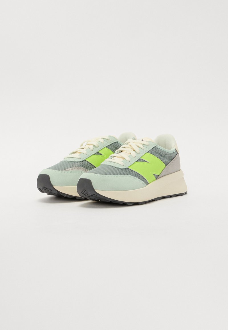 Grüne und graue Sneaker mit einer strukturierten Oberseite, kontrastierenden neon-grünen Akzenten, cremefarbenen Schnürsenkeln und einer schwarzen Gummisohle.