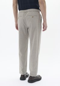 Pantalones gris claro con cinturilla elástica, que cuentan con dos bolsillos traseros con botones redondos y un diseño de pierna recta. Combinados con zapatos oscuros.