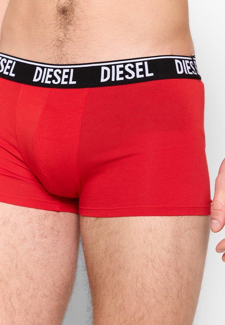 Gros plan sur une personne portant un boxer rouge Diesel avec une ceinture noire ornée de logos Diesel blancs.