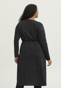 Schwarzes, langärmeliges Kleid aus strukturiertem, schimmerndem Stoff; tailliert; knielang mit geradem Schnitt und rundem Halsausschnitt.