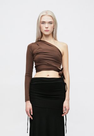 Haut marron à une épaule avec une accent noué, associé à une jupe noire froncée. Les deux vêtements sont en tissu lisse et extensible.