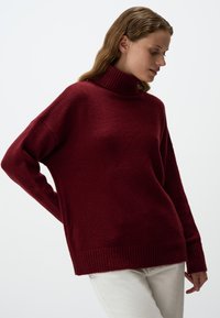 Bordeaux turtleneck trui van zacht, textuurstof. Heeft een losse pasvorm, geribbelde boorden en zoom. Gecombineerd met lichte broeken.