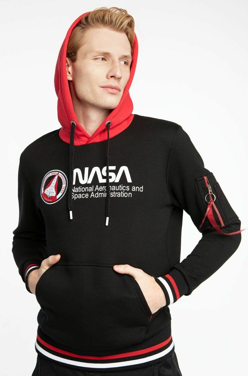 Hoodie noir avec des accents rouges et un grand logo NASA. Comprend une poche frontale et une poche zippée sur la manche. Tissu au toucher doux.