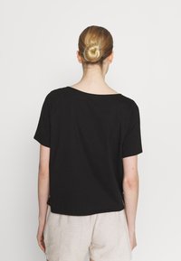 Černé tričko s krátkými rukávy a výstřihem ve tvaru člunu. Hladká bavlněná tkanina, volný střih, viditelné švy podél lemu.