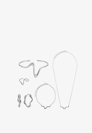 Ensemble de bijoux en argent avec un design ondulé, comprenant un bracelet manchette, une bague, des boucles d'oreilles, un bracelet chaîne et un collier sur fond blanc.