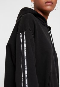 Sudadera con capucha negra con rayas verticales blancas que presenta el texto "LEVI'S". Tejido suave, corte relajado y diseño con bolsillo canguro.