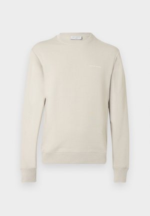 Ανοιχτό μπεζ φούτερ από μαλακό μείγμα βαμβακιού. Διαθέτει στρογγυλή λαιμόκοψη, μακριά μανίκια και μικρό λογότυπο στο στήθος. Υφή υφάσματος.