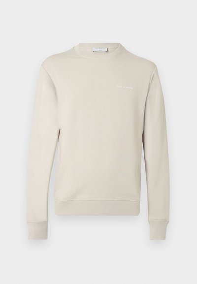 Ανοιχτό μπεζ φούτερ από μ αλακό μείγμα βαμβακιού. Διαθέτει στρογγυλή λαιμόκοψη, μακριά μανίκια και μικρό λογότυπο στο στήθος. Υφή υφάσματος.