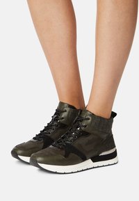 Sneakers verde altezza caviglia con pannelli testurizzati, design mimetico e dettagli neri. Suola in gomma bianca con un dettaglio metallico.