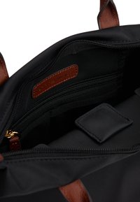 Black tote bag interior with brown leather accents, featuring a zipper pocket, an inner slip pocket, and smooth textures.