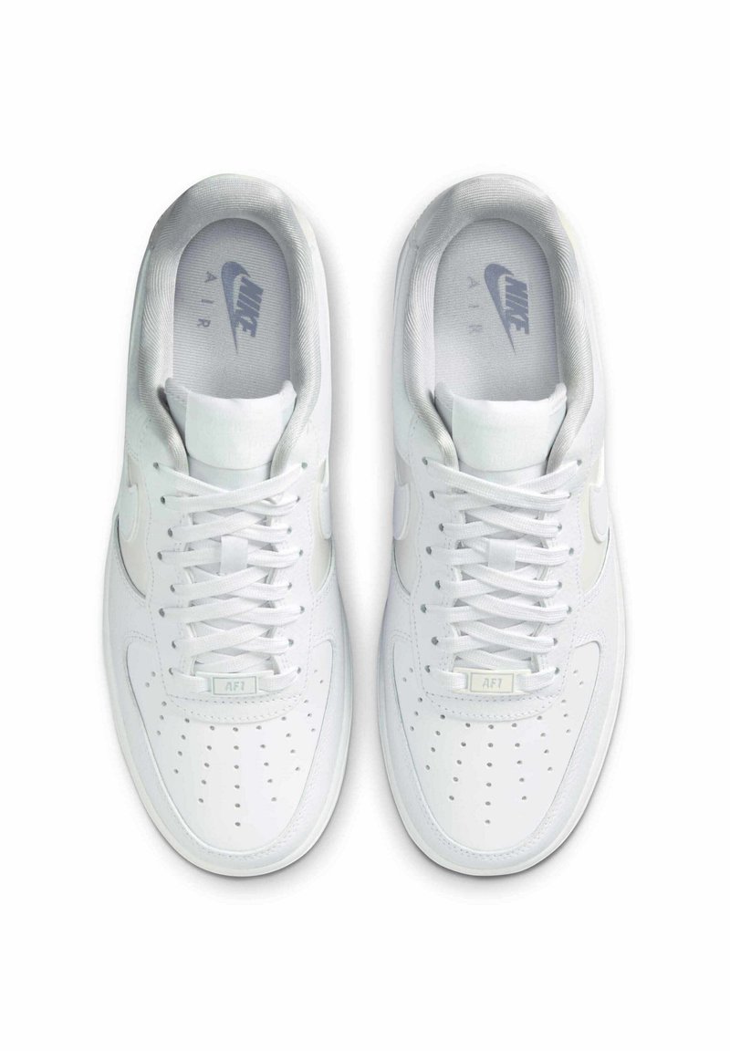 Witte leren sneakers met geperforeerde neus, platte veters, gevoerde kraag en Nike Air-logo op de binnenzolen en zijkanten. Overal een gladde textuur.