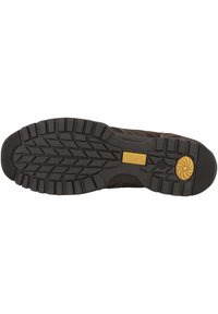 Braune Outdoor-Schuhsohle mit einer strukturierten schwarzen Gumm Oberfläche, die dicke Rillen und einen gelben kreisförmigen Akzent in der Nähe der Ferse aufweist.