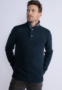 Pulover tricotat bleumarin cu guler cu nasturi, mansete și tiv cu dungi; prezintă un model texturat cu nuanțe subtile pe întreaga suprafață.