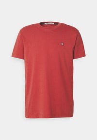 Rød bomulds T-shirt med korte ærmer, rund halsudskæring og et lille broderet logo på venstre bryst. Glat tekstur, klassisk pasform.