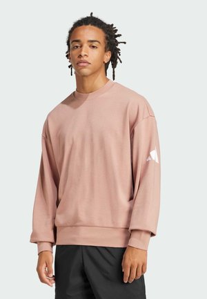 Ljusrosa oversized sweatshirt med långa ärmar, rund hals och en vit geometrisk design på vänster ärm. Mjuk texturerad tyg.
