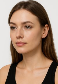 Små, runda stiftörhängen med silverfärgad yta, med en subtil strukturerad yta, bar av en modell med långt, rakt hår.