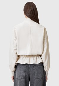 Lys beige læderjakke med en strammet talje, ribbede manchetter og en glat tekstur. Har et enkelt, skræddersyet design uden synligt hardware.