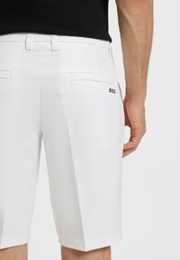 Pantaloni corti bianchi in tessuto liscio, con taglio dritto, due tasche posteriori e un logo nero "BOSS" sulla tasca destra.