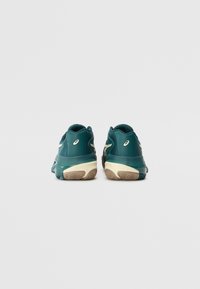 Türkisfarbene Sportschuhe mit einem schlanken Design, das ein glattes Obermaterial, eine gepolsterte Sohle und kontrastierende beigefarbene Akzente an der Ferse und der Außensohle aufweist.