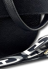 Sac à main en cuir noir au fini texturé, doté d'une bandoulière plate avec des lettrages blancs contrastants et des accents lisses.