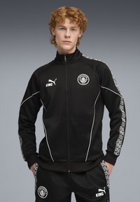 Czarny dres składający się z zapinanej na zamek kurtki z białymi akcentami, logo i wzorzystymi panelami bocznymi, połączony z pasującymi spodniami.