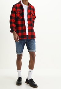Red and black checkered flannel shirt over a white t-shirt, paired with denim shorts and black shoes, complemented by white socks.
