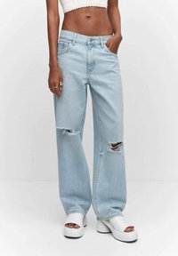Jeans de pierna ancha en azul claro con rasgaduras desgastadas, cinco bolsillos y cierre de botón. Combinados con zapatos de plataforma blancos.