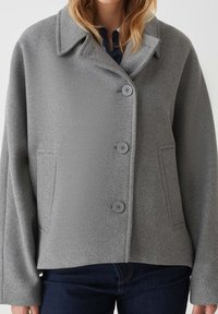 Giacca in misto lana grigia con colletto a rever, quattro bottoni e due tasche frontali. Presenta un tessuto testurizzato e una vestibilità rilassata.