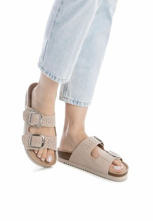 Sandalias de ante beige con correas anchas, con perforaciones y hebillas plateadas. Plantilla de corcho con suela de goma blanca. Llevadas con denim claro.