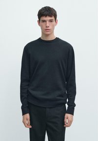 Maglione nero lavorato a maglia con scollo tondo e collo a coste, abbinato a pantaloni scuri a righe. Tessuto liscio, design aderente, dettagli minimali.