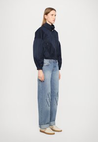 Marineblå, lett, cropped jakke med høy krage og elastiske mansjetter. Brukt med lyseblå, løstsittende jeans med trykte detaljer.