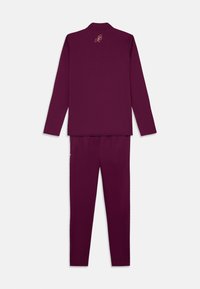 Σκοτεινά μωβ αθλητικά ρούχα που περιλαμβάνουν ένα μακριμάνικο μ�πλουζάκι με γιακά και παντελόνι, και τα δύο από μαλακό, λείο ύφασμα. Κεντημένο λογότυπο στην πλάτη.