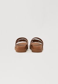 Brune sandaler med to brede stropper og åpen bak, med en jevn tekstur og flat gummisåle, sett bakfra.
