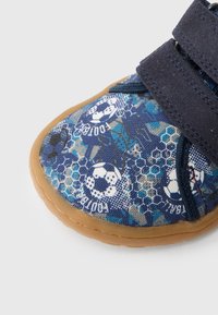 Modrá detská topánka z textúrovaného materiálu s motívom futbalovej lopty a hexagónovým vzorom. Zapínanie na suchý zips, gumová podrážka a zaoblená špička.