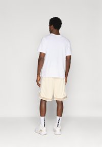 Balta īsām piedurknēm t-krekls, bēšas acs šortos ar sānu ziedu rakstu, baltas sporta kurpes un melnas svītrains zeķes. Aizmugures skats.