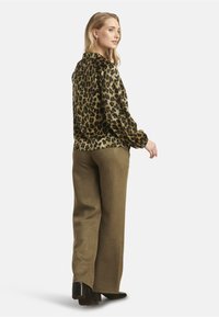 Leopard print blouse with long sleeves, paired with olive green wide-leg trousers in a soft fabric, and black heeled shoes for added contrast.