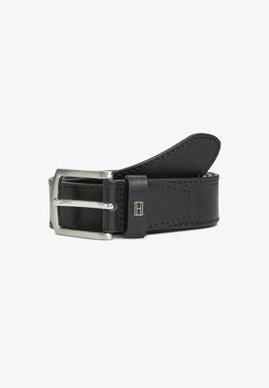 Cinturón de cuero negro con hebilla rectangular plateada, costuras visibles y pequeño logo de metal en el lazo del cinturón, enrollado sobre fondo blanco.